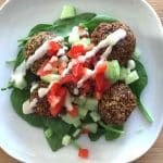 Tallrik med falafelbollar, tomat, selleri och sås på en bädd av spenat.