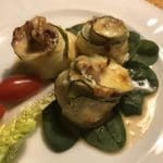 Tre zucchini-rullar fyllda med ingredienser, serverade på en tallrik med spenat och körsbärstomater.