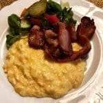En tallrik med äggröra, bacon och grönsallad på en vit tallrik.