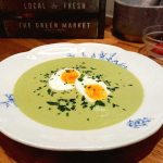 En skål med broccolisoppa som har halverade ägg och grönsaker som garnering.