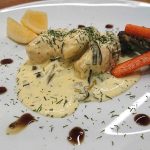 Fiskbullar i en syrlig sås serverade med grönsaker och citronklyftor på en tallrik.