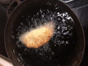 Friterad degbit som bubblar i het olja i en gjutjärnspanna.