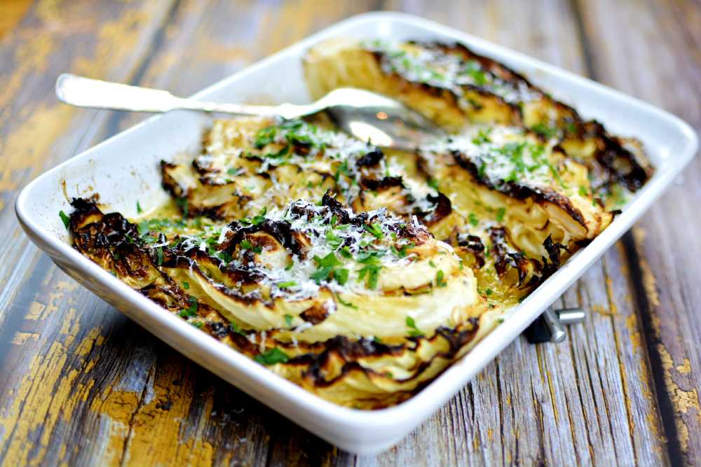 Spetskål i ugn 7 Ugnsbakad spetskål med riven parmesan och persilja på toppen. Allt ligger i en vit ugnsform på ett gammal träbord