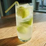 Ett glas med limebitar och sodavatten, med ett sugrör, placerat på ett bord.