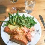 En tallrik med lax, grönsaker och ett glas vitt vin på ett bord.
