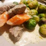 En tallrik med dillkött, morötter och brysselkål i en krämig sås.