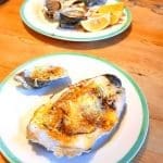 Grillade ostron på en tallrik med citronskivor och en annan tallrik i bakgrunden.