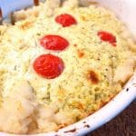En gratäng med en krämig yta, körsbärstomater och dill i en vit ugnsform.