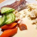 En tallrik med kokt kött, morötter, gurka och blomkål i sås.