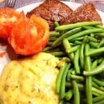 En tallrik med stekt kött, gröna bönor, tomater och potatispuré.