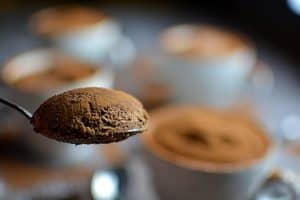 En sked med kakaopulver framför flera koppar med dessert som har ett lager av kakaopulver.