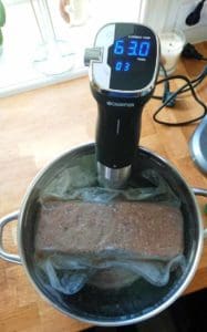 Sous vide-cirkulator placerad i en kastrull med en förpackad matbit som värms upp.