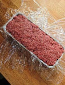 Köttfärslimpa formad i en aluminiumform och inlindad i plastfolie.
