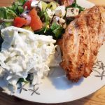 Grillad yoghurtmarinerad kycklingfilé serverad med sallad och vit sås på en tallrik.
