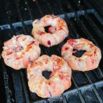 Fyra grillade lökringar inlindade i bacon på en grill.