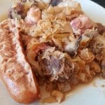 En tallrik med kött, surkål och en korv på sidan av rätten.