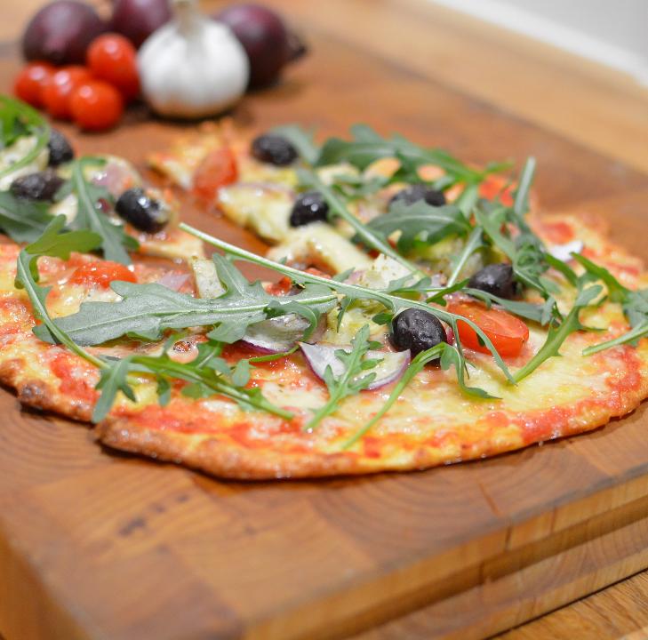 Supergod pizzasallad 13 En pizza med tomater, oliver och ruccola på en träskärbräda.