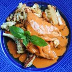 En portion kyckling med garam masala sås och rostad blomkål på en blå tallrik.