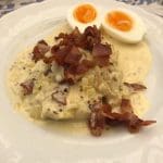 En tallrik med en maträtt bestående av bacon, sås och halvmjuka ägg.