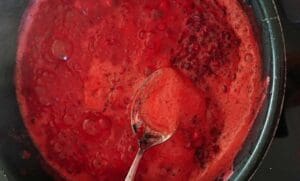 Kastrull med röd fruktgröt som kokar, med en sked i.