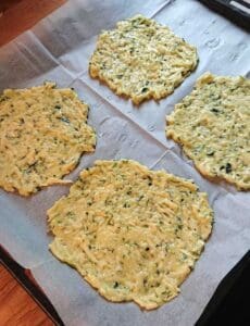 Fyra platta zucchiniplättar på bakplåtspapper, redo för gräddning.