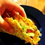 En hand som håller en taco fylld med grönsaker på en blå tallrik.