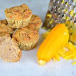 Zucchinimuffins staplade bredvid en rivjärn och riven zucchini på en yta.