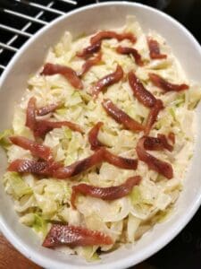 En gratäng med vitkål och skivor av bacon i en vit ugnsform.