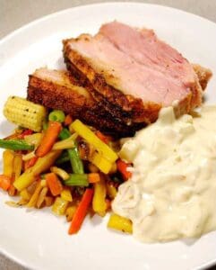 En tallrik med ungsstekt sidfläsk, grönsaksblandning och en krämig sås.