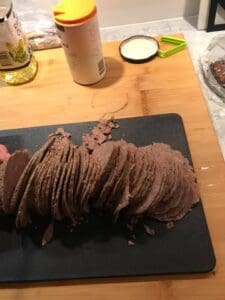 Skivor av en köttprodukt placerade på en svart skärbräda med en hand som håller en skiva.