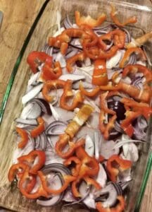 Ugnsform med skivor av kassler, rödlök och skivor av röd paprika.
