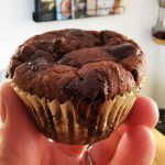 En person håller en chokladmuffin med chokladbitar i handen.