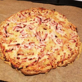 Supergod pizzasallad 14 En rund pizza med skinka och ost på en bakplåt.