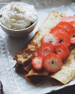 Tre pannkakor på en tallrik med skivade jordgubbar och en skål med grädde.