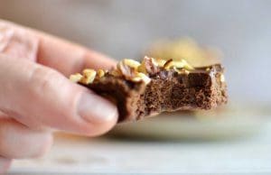 En hand håller en bit hasselnötsbrownie med en bit tagen från den.