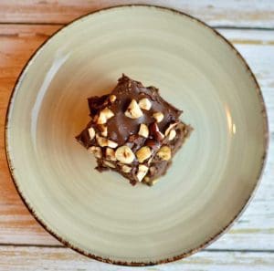 En bit hasselnötsbrownie med hackade nötter på toppen, placerad på en grön tallrik.