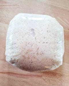 En inplastad brödliknande produkt med en kvadratisk form på en träyta.
