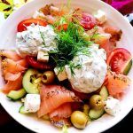 En tallrik med sallad som innehåller rökt lax, tomater, gurka, oliver och dillmajonnäs.