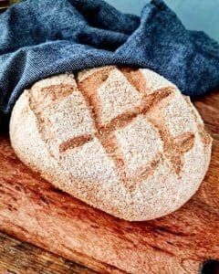 Bröd med en grov yta och snittat mönster, delvis täckt av en grå duk.