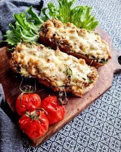 Falskt surdegsbröd med fyllning, toppat med ost, och grillade tomater på en skärbräda.