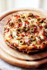 Pizza med oliver, grönsaker och ost på en träskärbräda.