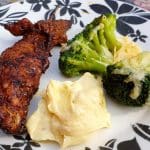 Grillad kyckling på spett med broccoli och en klick sås på en tallrik med blommönster.