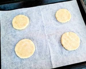 Fyra runda kakor placerade på bakplåtspapper på en plåt.