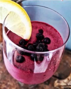 En smoothie i ett glas med blåbär och en citronskiva på kanten.