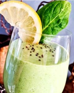 Grön smoothie i ett glas med en skiva citron och spenatblad på toppen.