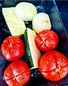 Röda tomater, zucchini och lök i en glasbehållare.