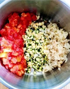 En skål med hackad tomat, zucchini och lök i separata sektioner.