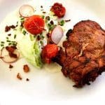 En tallrik med grillad kyckling, grönsaker och sås, inklusive tomater och sallad.