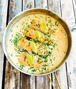 Laxfiléer i en panna med kokosgrädde och limeklyftor, garnerad med gräslök.