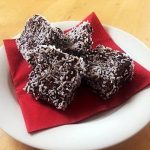 En tallrik med chokladrutor täckta av kokosflingor på en röd servett.